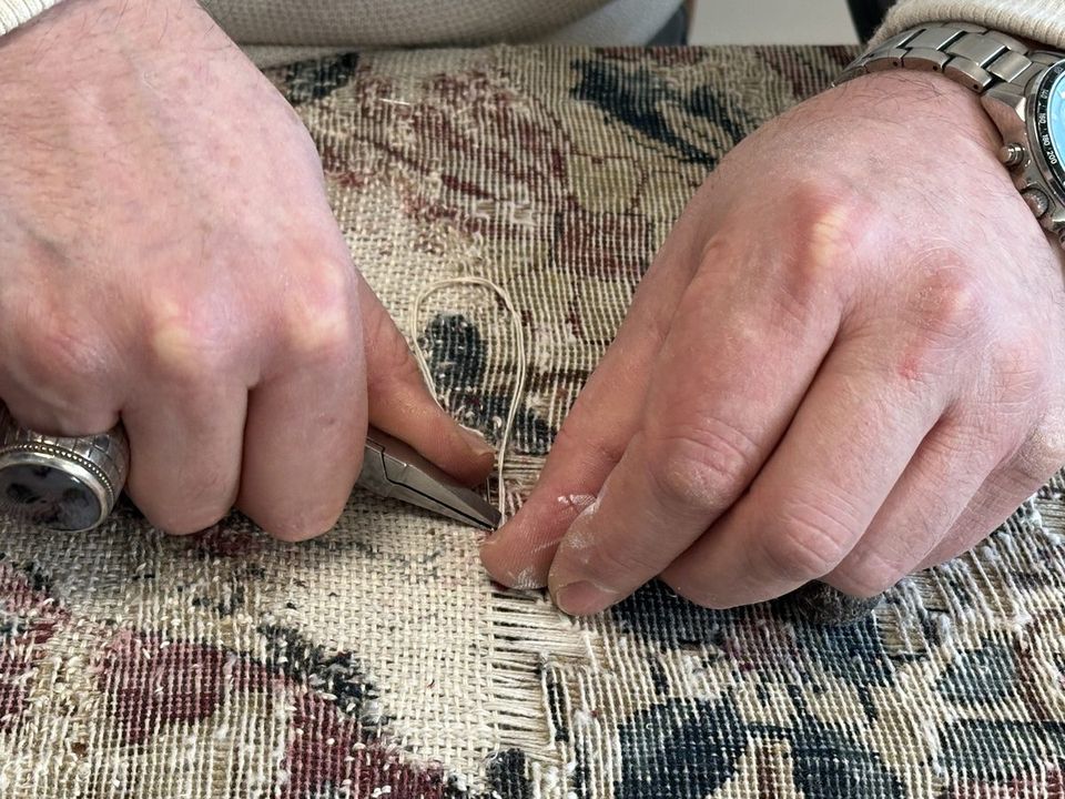 A craftsman's hands rebuilding the warp threads of a worn area with tweezers