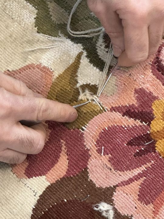 Needle and wool being passed through a floral Aubusson tapestry