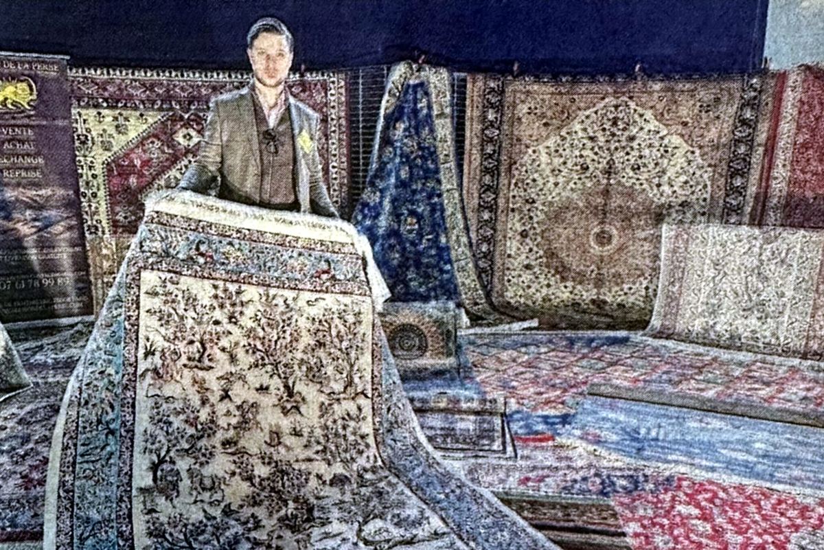 Adrien Mignaton presenting a silk rug decorated with trees and animals, in front of hanging Oriental rugs