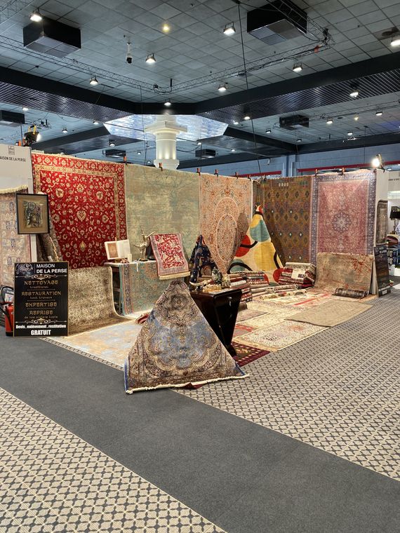 La Maison de la Perse's stand at a fair: hanging Persian rugs, silk rugs and objets d'art