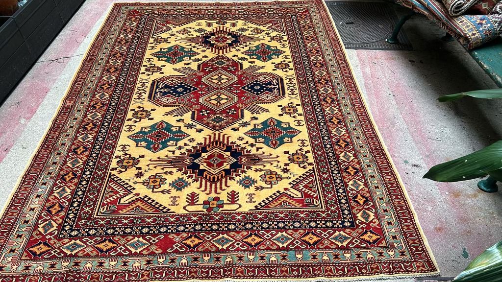 Hand-knotted Kazak rug with a yellow field, red, blue and green geometric medallions and a wide red border