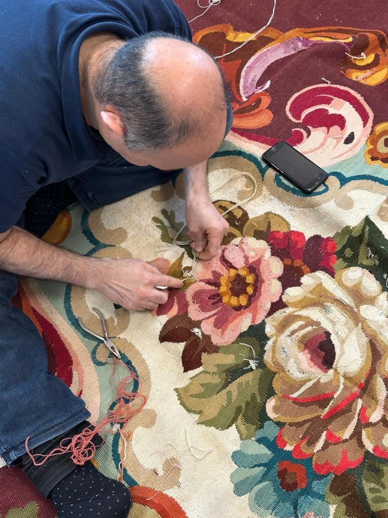 A La Maison de la Perse craftsman restoring a floral-patterned rug by hand